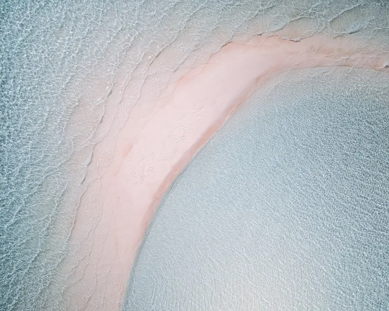 Aerial view of a pink-sand shoreline curving into turquoise water