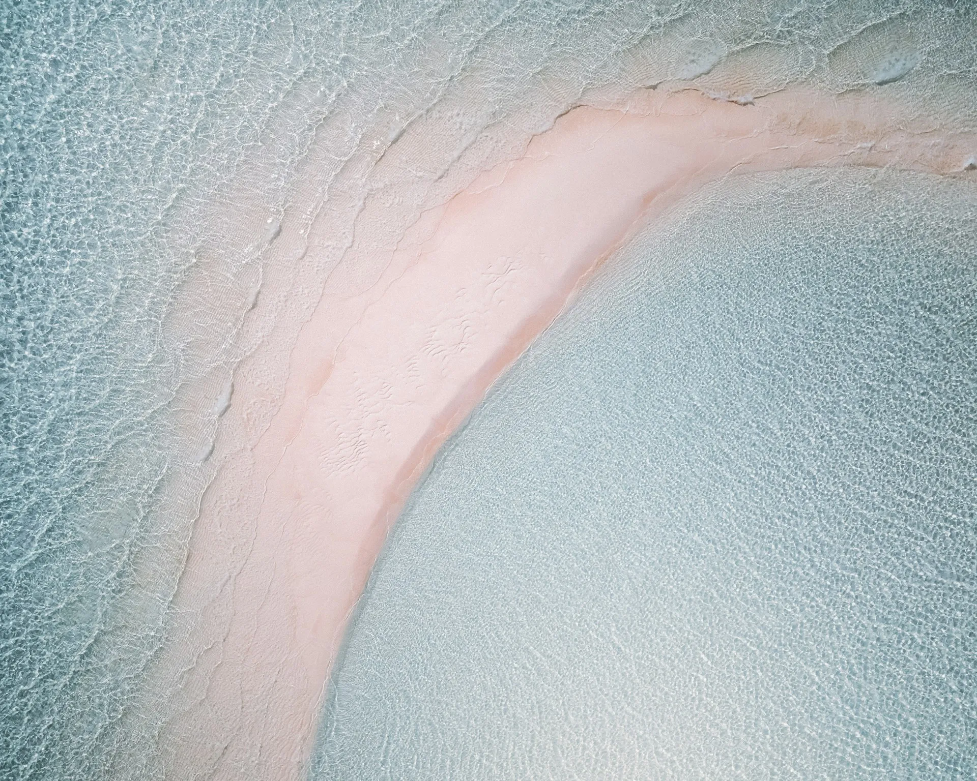 Aerial view of a pink-sand shoreline curving into turquoise water